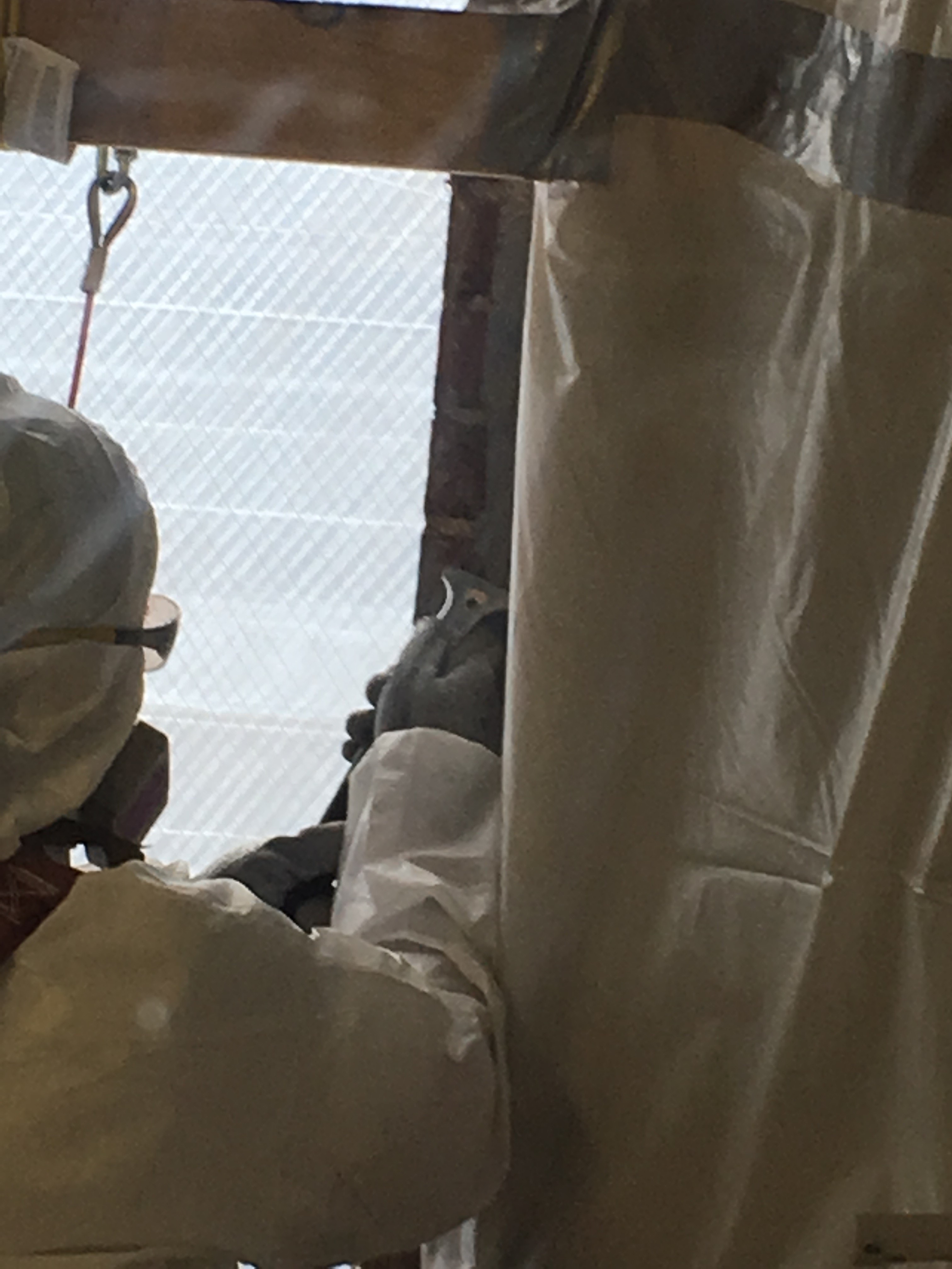 A worker in full hazmat (eye protection, respiratory protection, tyvek coveralls, gloves) scrapes PCB/Asbestos caulk from brick.